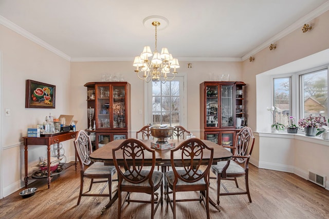 dining area with light wood-style flooring, visible vents, baseboards, ornamental molding, and an inviting chandelier