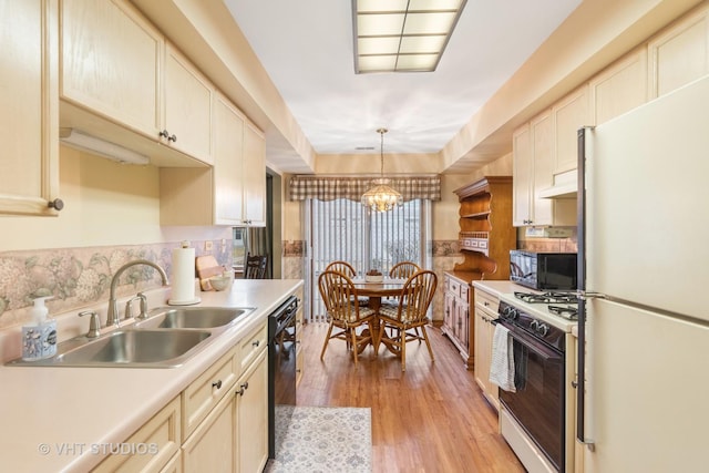 kitchen featuring light wood finished floors, a sink, light countertops, black appliances, and a notable chandelier