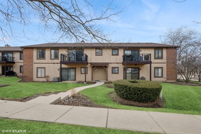 view of front of house with a balcony, a chimney, a front lawn, and central AC