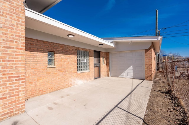 exterior space featuring a garage, driveway, brick siding, and fence