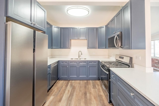 kitchen with appliances with stainless steel finishes, gray cabinets, light countertops, light wood-style floors, and a sink