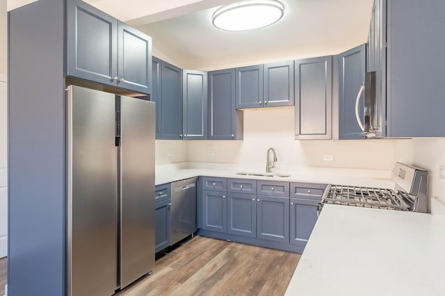 kitchen with appliances with stainless steel finishes, light wood-type flooring, light countertops, and a sink