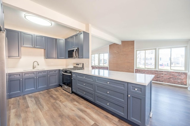 kitchen with stainless steel appliances, light countertops, light wood-style floors, a sink, and a peninsula