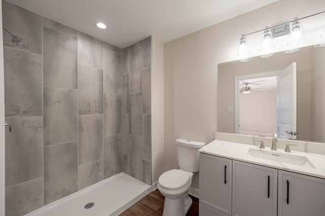 full bathroom with toilet, a ceiling fan, vanity, wood finished floors, and tiled shower