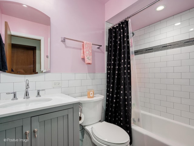 bathroom with toilet, vanity, tile walls, wainscoting, and shower / bath combo with shower curtain