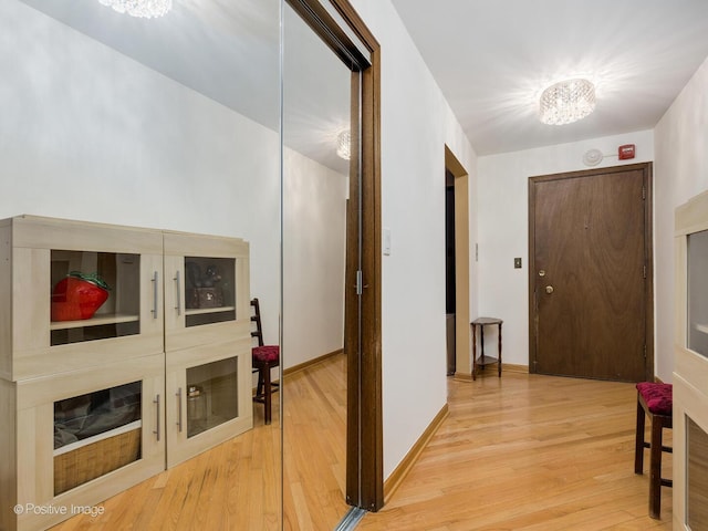 hallway with baseboards, wood finished floors, and an inviting chandelier