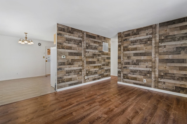 spare room featuring visible vents, baseboards, an inviting chandelier, and wood finished floors