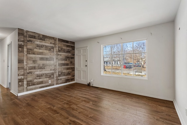 empty room with wooden walls, an accent wall, baseboards, and wood finished floors