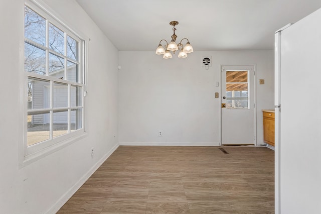 unfurnished room featuring light wood-type flooring, baseboards, and a notable chandelier