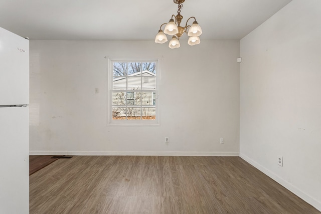 unfurnished dining area with baseboards, a notable chandelier, and wood finished floors