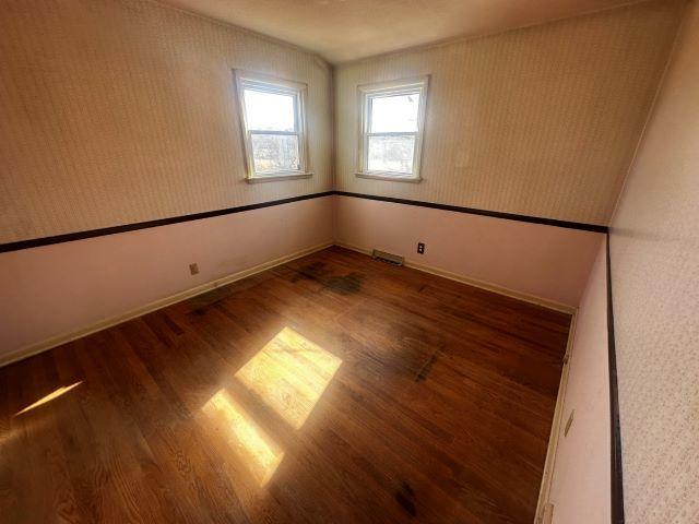 unfurnished room featuring wood finished floors, visible vents, and baseboards