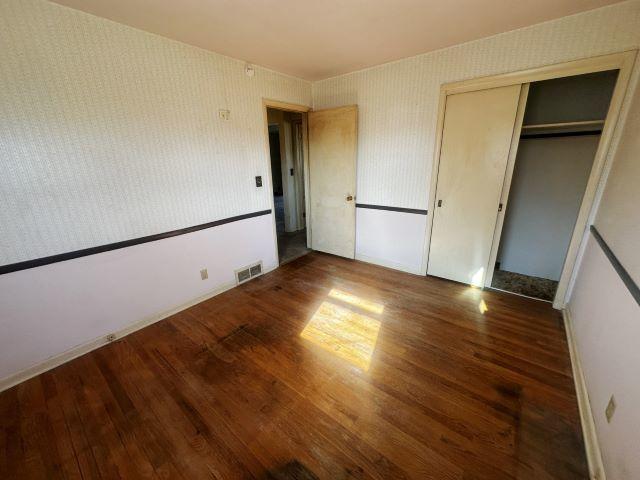 unfurnished bedroom with wallpapered walls, visible vents, and wood finished floors