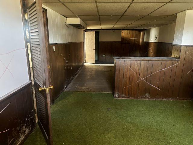 bar featuring a drop ceiling, wood walls, wainscoting, and carpet flooring