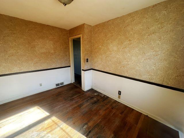 unfurnished room featuring wainscoting, dark wood finished floors, visible vents, and wallpapered walls