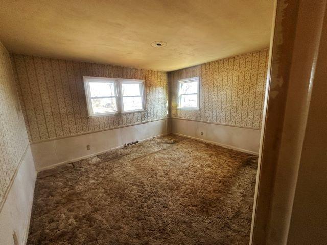 carpeted empty room featuring a wainscoted wall, visible vents, and wallpapered walls