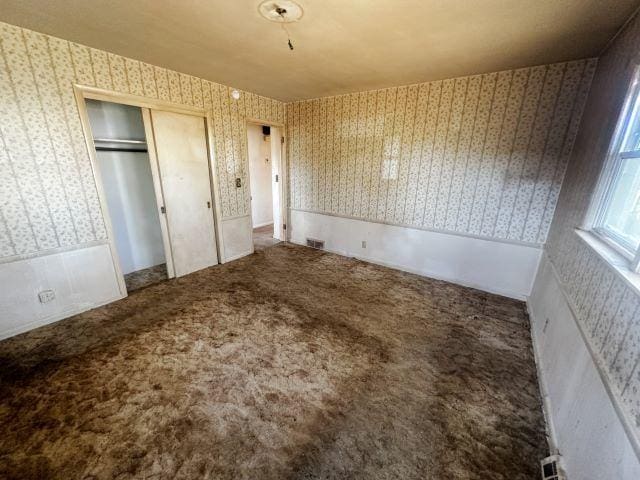 unfurnished bedroom with wallpapered walls, carpet, visible vents, and a closet