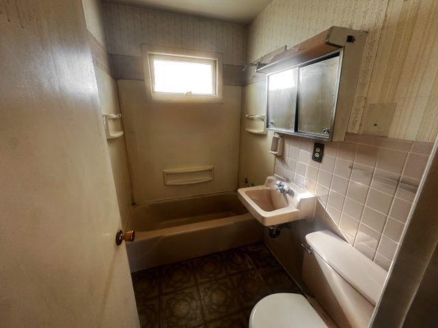 bathroom with toilet, a sink, tile walls, walk in shower, and wallpapered walls