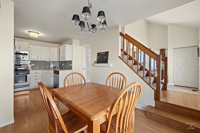 dining area with baseboards, stairway, an inviting chandelier, vaulted ceiling, and light wood-style floors