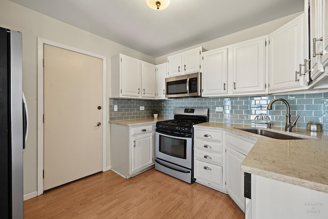 kitchen featuring stainless steel appliances, a sink, white cabinets, backsplash, and light wood finished floors