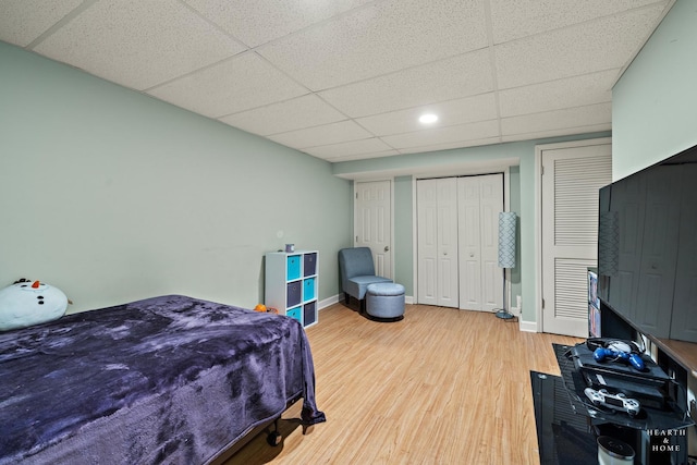 bedroom featuring a drop ceiling, two closets, baseboards, and wood finished floors