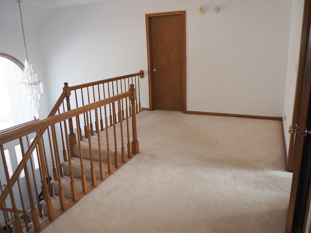 corridor with baseboards, carpet flooring, a notable chandelier, and an upstairs landing