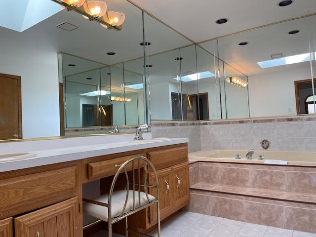 bathroom with a skylight, double vanity, a sink, tile patterned flooring, and a bath