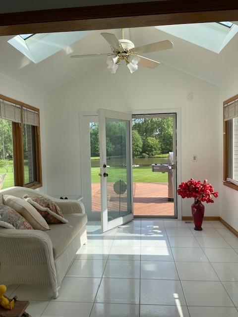 doorway to outside featuring lofted ceiling with skylight, ceiling fan, baseboards, and light tile patterned floors