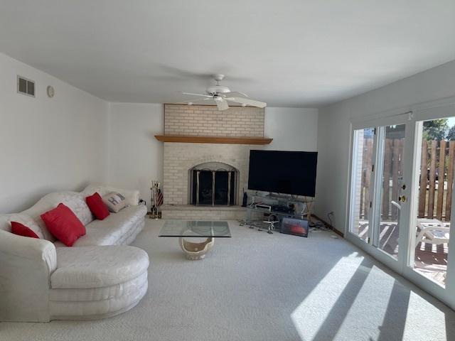 living room featuring a brick fireplace, carpet flooring, visible vents, and a ceiling fan