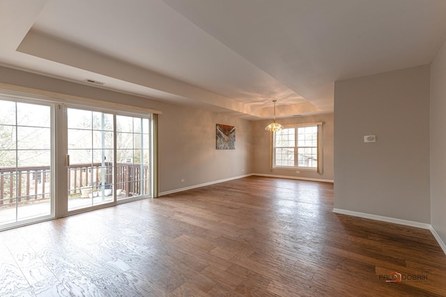 unfurnished room featuring a chandelier, wood finished floors, visible vents, baseboards, and a raised ceiling