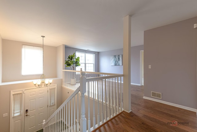 hallway featuring a notable chandelier, visible vents, an upstairs landing, wood finished floors, and baseboards