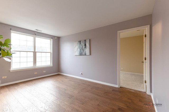 spare room featuring baseboards, visible vents, and wood finished floors