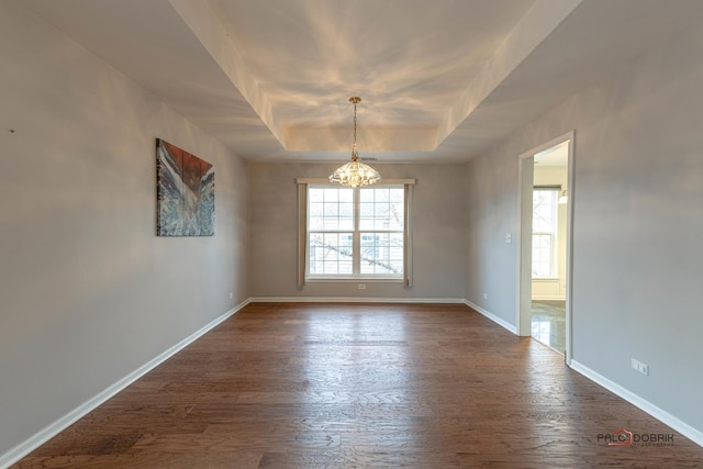 spare room with dark wood-style floors, baseboards, a tray ceiling, and a notable chandelier