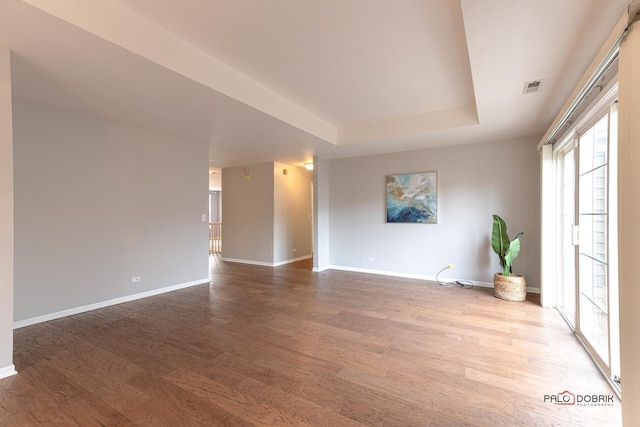 unfurnished room with a raised ceiling, visible vents, baseboards, and wood finished floors