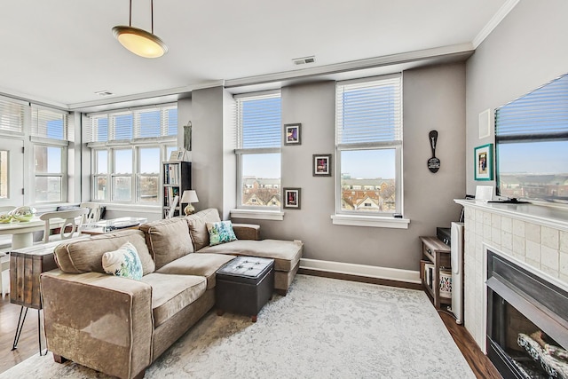 living room featuring visible vents, baseboards, a tiled fireplace, wood finished floors, and crown molding