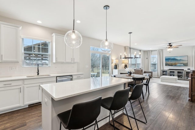 kitchen with dark wood-style floors, stainless steel dishwasher, decorative backsplash, open floor plan, and a sink