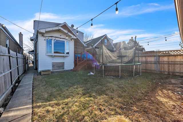 rear view of house with a fenced backyard, a trampoline, and a yard