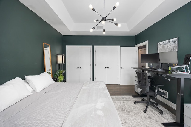 bedroom with a notable chandelier, wood finished floors, visible vents, a tray ceiling, and two closets