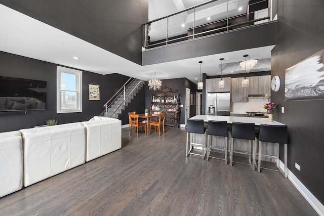 living area with a towering ceiling, baseboards, stairway, and dark wood-style flooring