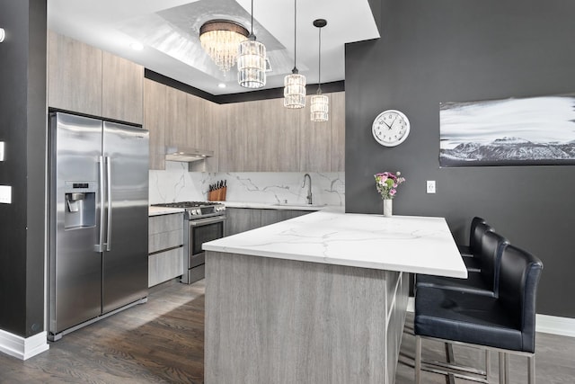 kitchen featuring modern cabinets, light stone counters, stainless steel appliances, under cabinet range hood, and a sink