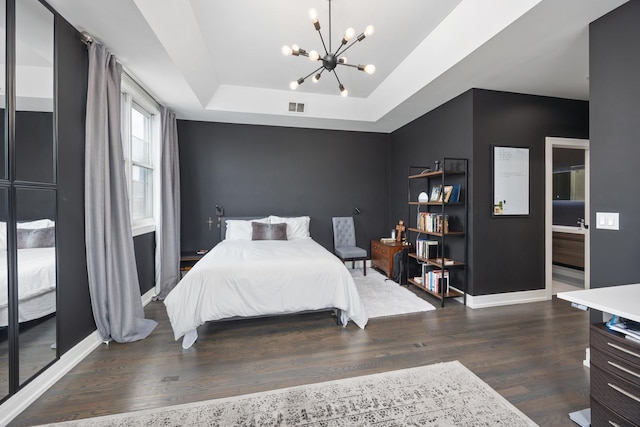 bedroom featuring a tray ceiling, visible vents, an inviting chandelier, wood finished floors, and baseboards