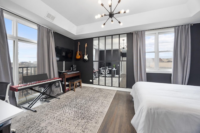 bedroom featuring wood finished floors, visible vents, baseboards, a tray ceiling, and an inviting chandelier