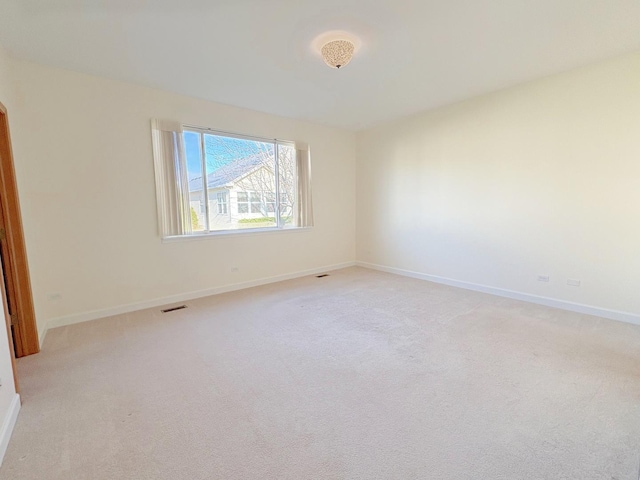 empty room featuring light colored carpet, visible vents, and baseboards