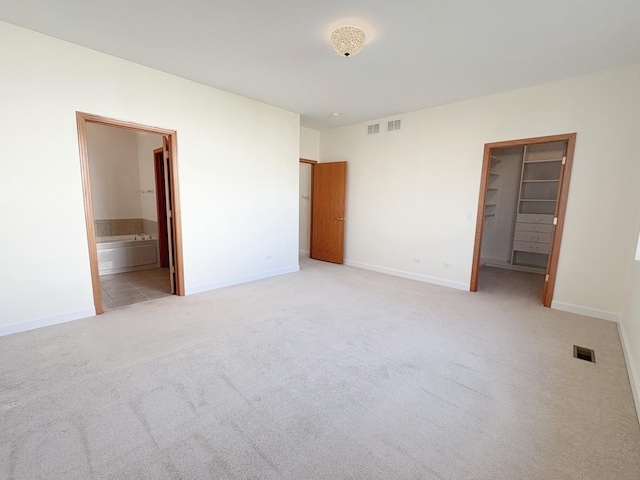 unfurnished bedroom with light carpet, baseboards, visible vents, connected bathroom, and a spacious closet