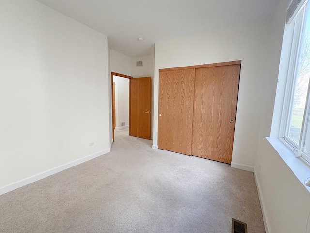 unfurnished bedroom featuring a closet, visible vents, light carpet, and baseboards