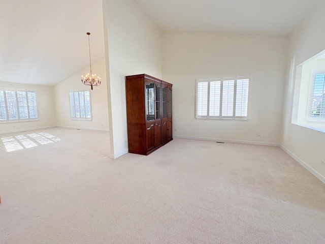 empty room featuring light carpet, high vaulted ceiling, baseboards, and a notable chandelier