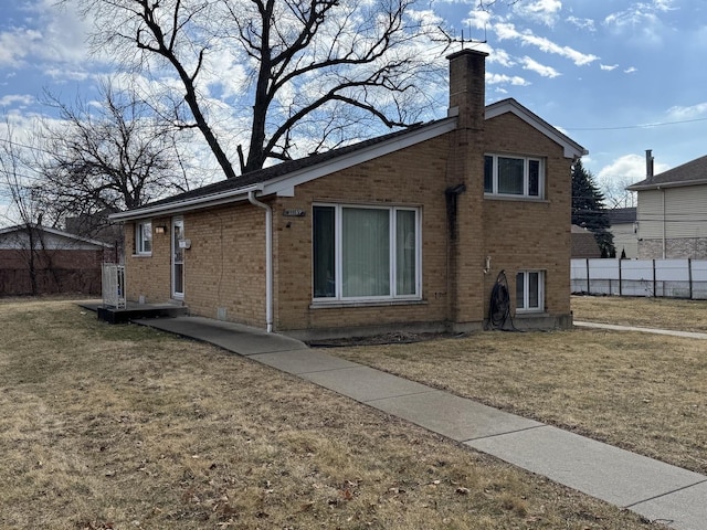 view of property exterior featuring brick siding, fence, a chimney, and a lawn