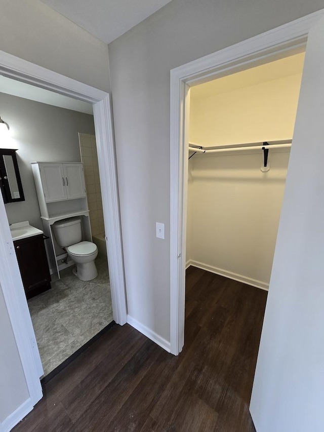 bathroom with toilet, wood finished floors, vanity, baseboards, and a walk in closet