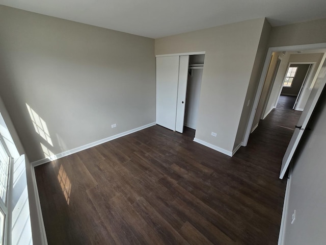 unfurnished bedroom featuring dark wood-style floors, a closet, and baseboards