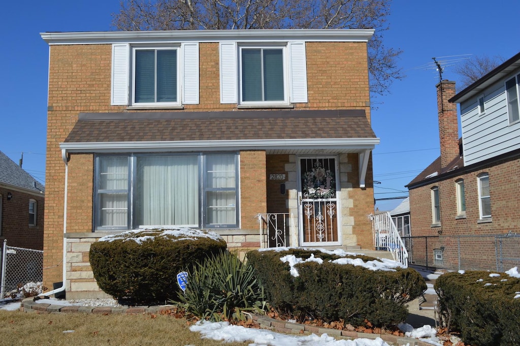 view of front of home with covered porch, a shingled roof, stone siding, and fence