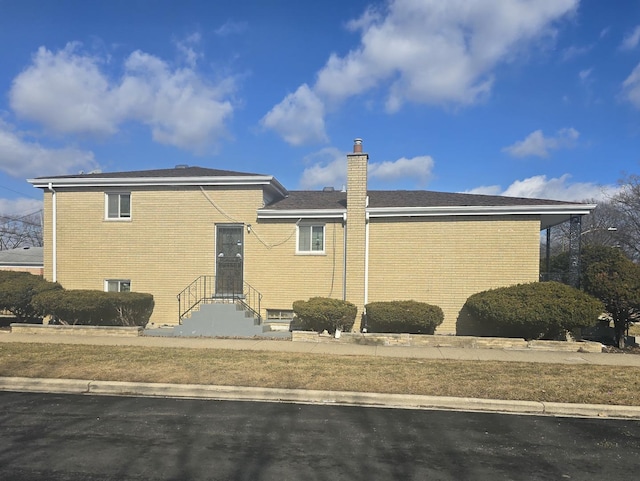 exterior space with entry steps, a chimney, and brick siding